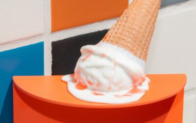 Ice cream cone tipped over with melted ice cream spilling onto an orange holder, set against a colorful tiled background, illustrating the theme of change and adaptation in a playful manner.