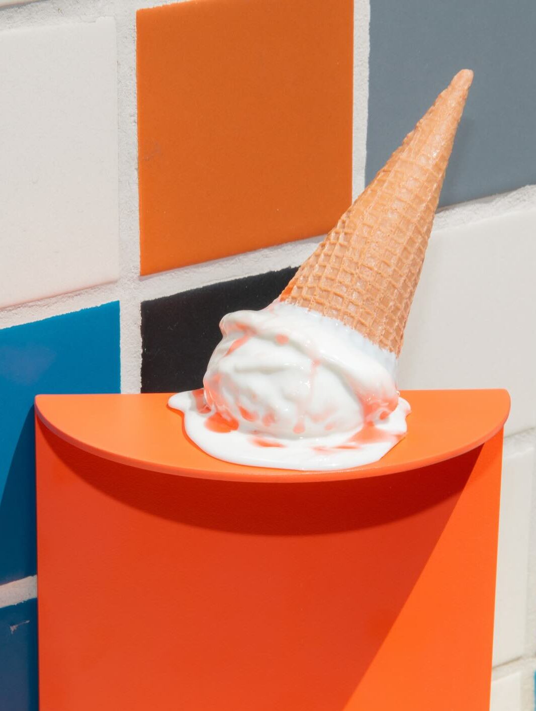 Ice cream cone with melting ice cream on an orange surface against a colorful tiled background, illustrating the theme of indulgence and creativity in visual marketing.