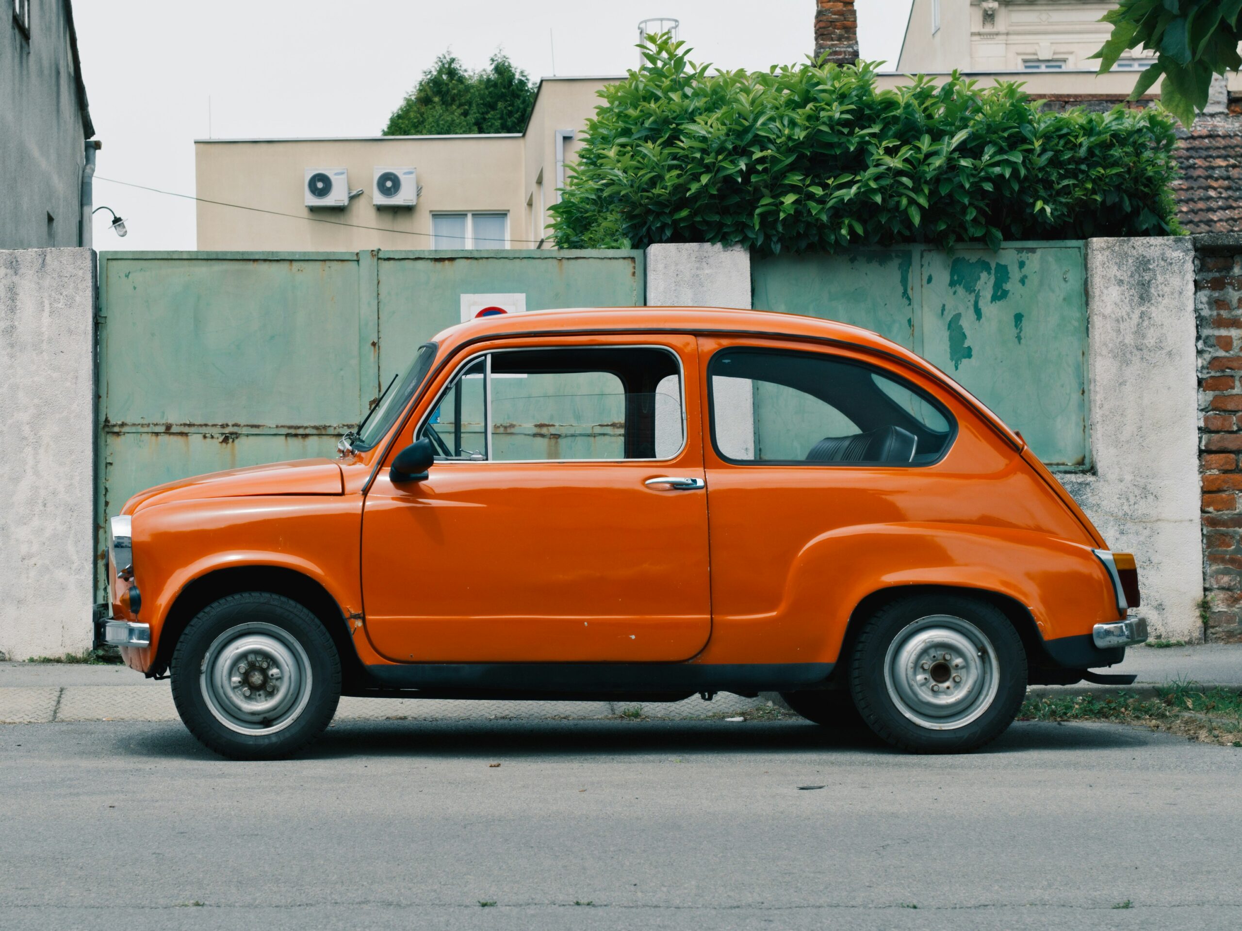 Orange vintage car parked beside a weathered green fence, reflecting themes of nostalgia and urban environment, relevant to brand strategy and execution discussions.